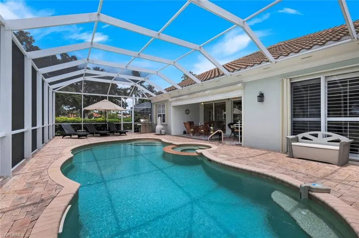 Screened outdoor pool area featuring a freeform swimming pool, integrated spa, and brick paver decking