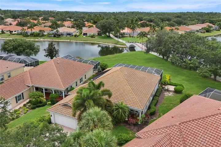 Lakeside property featuring a tile roof, screened lanai, manicured landscaping, and an attached garage