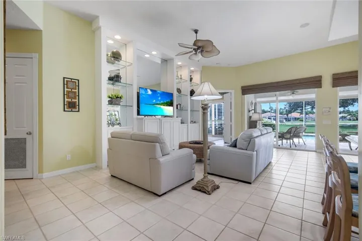 Living area featuring built-in white cabinetry with glass shelving and integrated lighting, a ceiling fan, and tile flooring