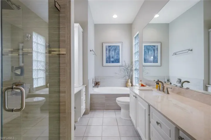 Built-in soaking tub with tile surround, glass block window, and light-toned wall tile