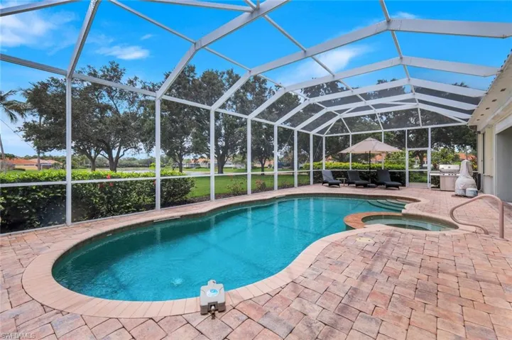 Expansive lakefront setting with verdant grass, mature trees, and residential properties featuring screened enclosures and tile roofs bordering the water