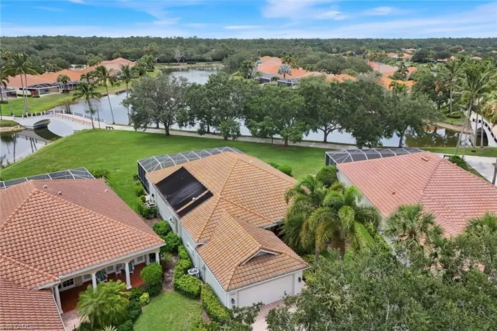 Aerial overview of a residential community featuring extensive water features, mature landscaping, numerous properties with screened-in pools, and red tile roofing