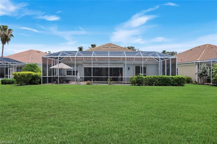 Expansive green lawn bordering a stucco exterior home featuring a screened lanai enclosure with a tile roof