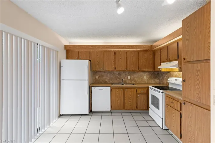 Kitchen with white appliances, tasteful backsplash, light tile patterned flooring, brown cabinets, and a textured ceiling