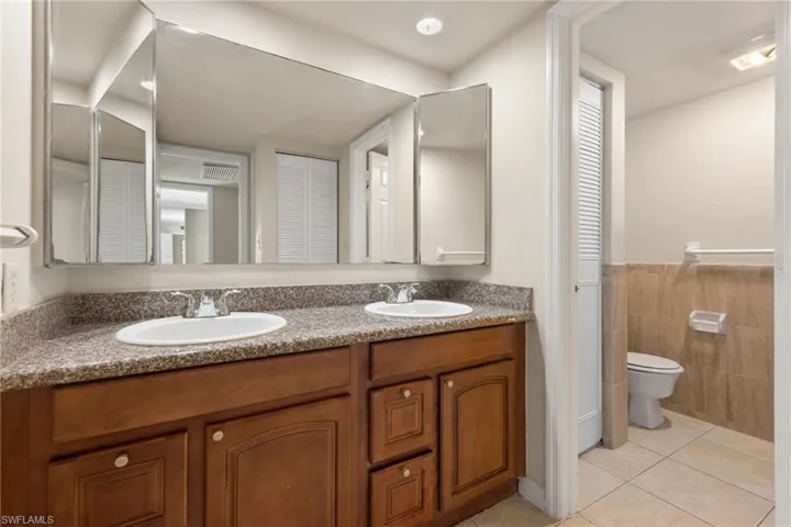 Bathroom with a closet, double vanity, light tile patterned flooring, tile walls, and a wainscoted wall