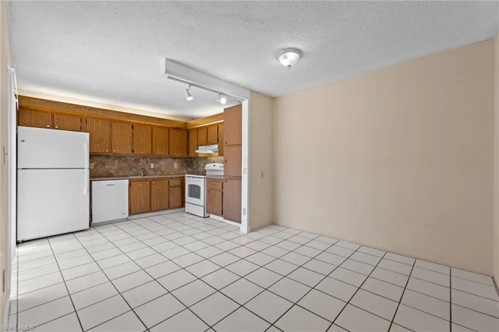 Kitchen featuring white appliances, a textured ceiling, light tile patterned flooring, brown cabinetry, and backsplash