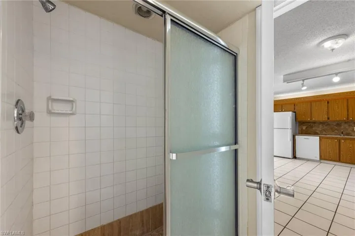 Bathroom with a shower stall, a textured ceiling, light tile patterned floors, tasteful backsplash, and rail lighting
