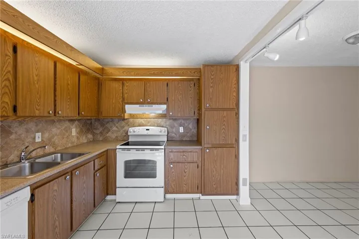Kitchen featuring white appliances, a textured ceiling, decorative backsplash, light countertops, and light tile patterned floors