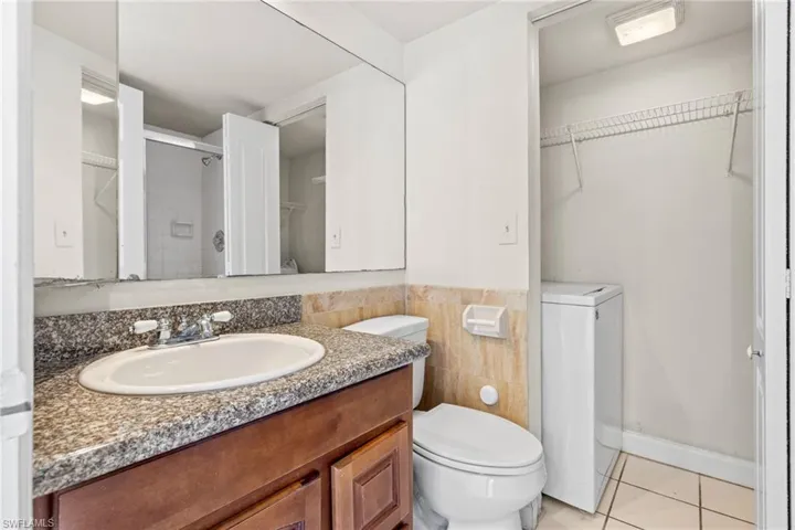 Bathroom featuring a walk in closet, light tile patterned flooring, washer / clothes dryer, a shower stall, and vanity