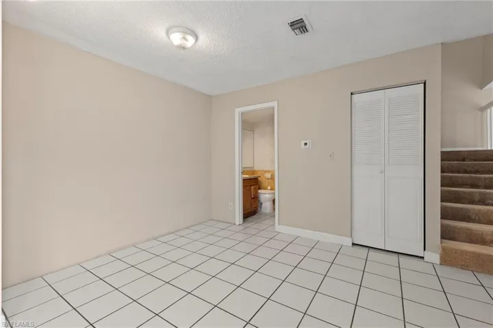 Unfurnished bedroom featuring a textured ceiling, ensuite bathroom, light tile patterned floors, and a closet