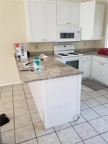 Kitchen featuring white appliances, white cabinetry, light stone countertops, and light tile patterned floors