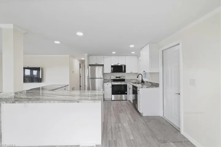 Kitchen with crown molding, appliances with stainless steel finishes, light stone counters, light wood-type flooring, and white cabinets
