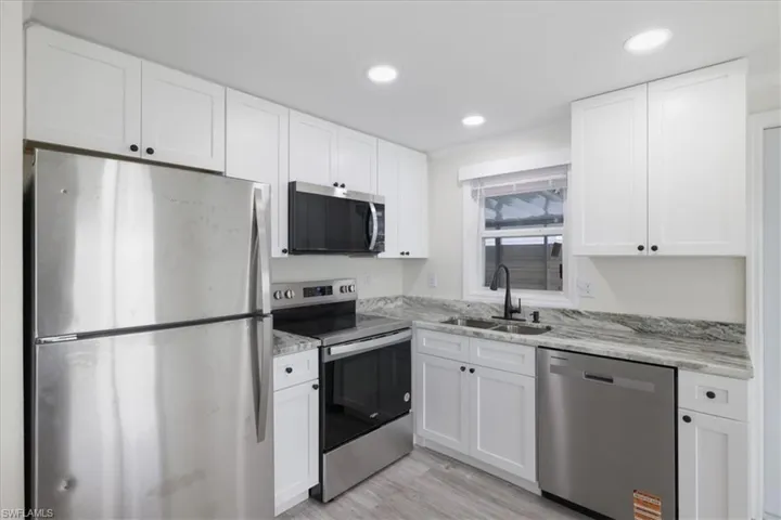 Kitchen with appliances with stainless steel finishes, white cabinets, recessed lighting, light wood-style floors, and light stone counters