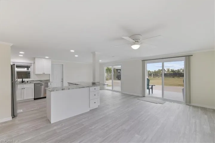 Kitchen with white cabinetry, a kitchen island, light stone countertops, appliances with stainless steel finishes, and light wood finished floors