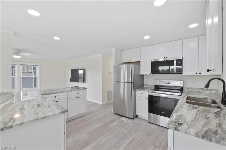Kitchen featuring appliances with stainless steel finishes, light stone counters, white cabinets, light wood-style floors, and recessed lighting