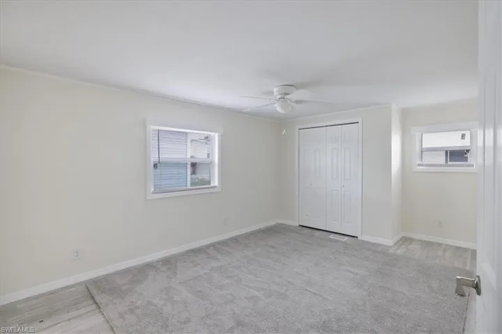 Unfurnished bedroom with crown molding, ceiling fan, a closet, multiple windows, and light carpet