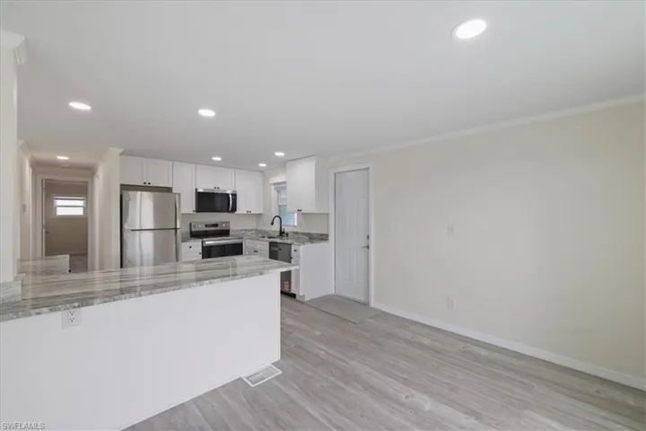 Kitchen featuring appliances with stainless steel finishes, a peninsula, light stone counters, recessed lighting, and white cabinets