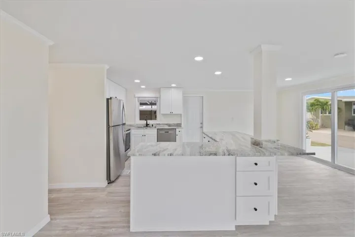 Kitchen featuring ornamental molding, stainless steel appliances, white cabinets, light stone counters, and a peninsula