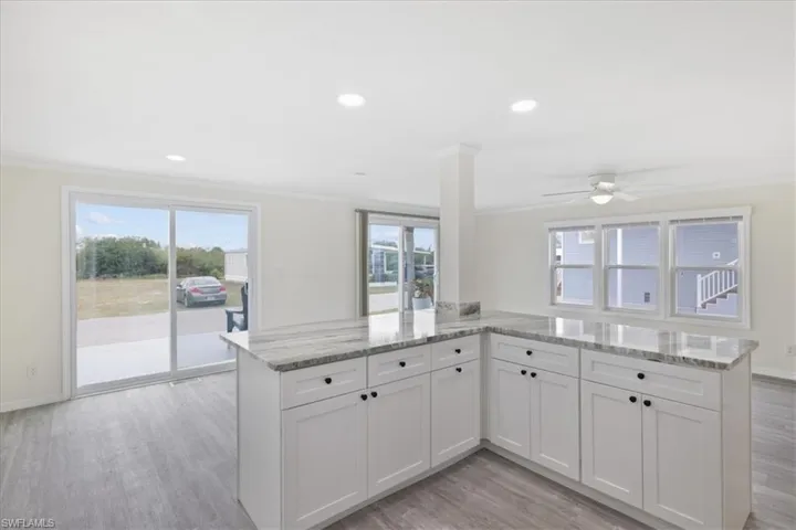 Kitchen with white cabinets, light stone counters, light wood-style floors, ornamental molding, and recessed lighting