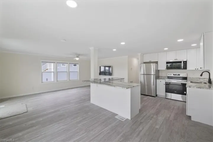 Kitchen featuring appliances with stainless steel finishes, light stone counters, white cabinets, open floor plan, and recessed lighting