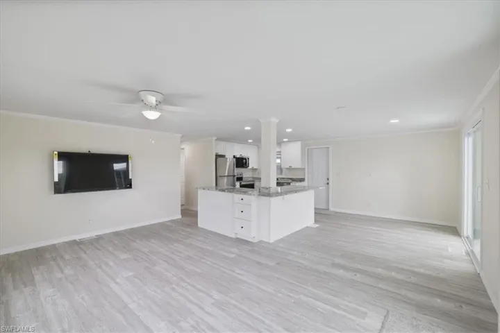 Kitchen featuring open floor plan, white cabinets, ornamental molding, an island with sink, and light wood-style floors
