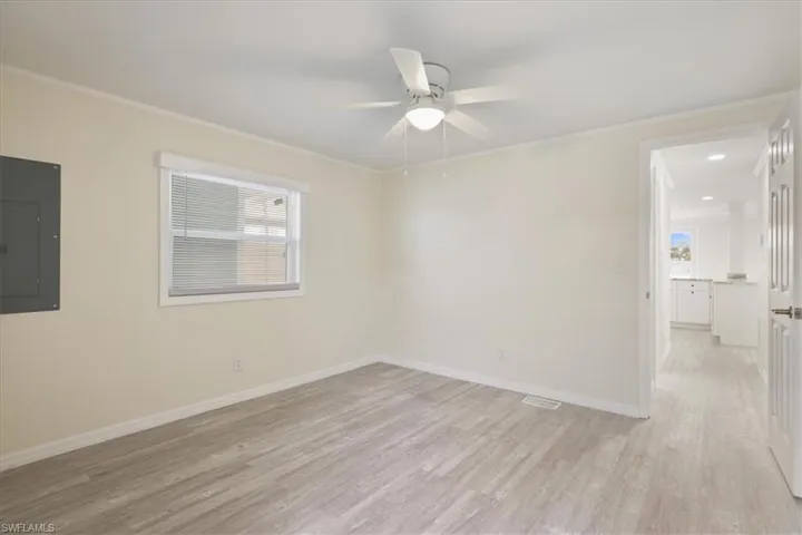 Unfurnished room featuring electric panel, light wood-type flooring, crown molding, a ceiling fan, and plenty of natural light