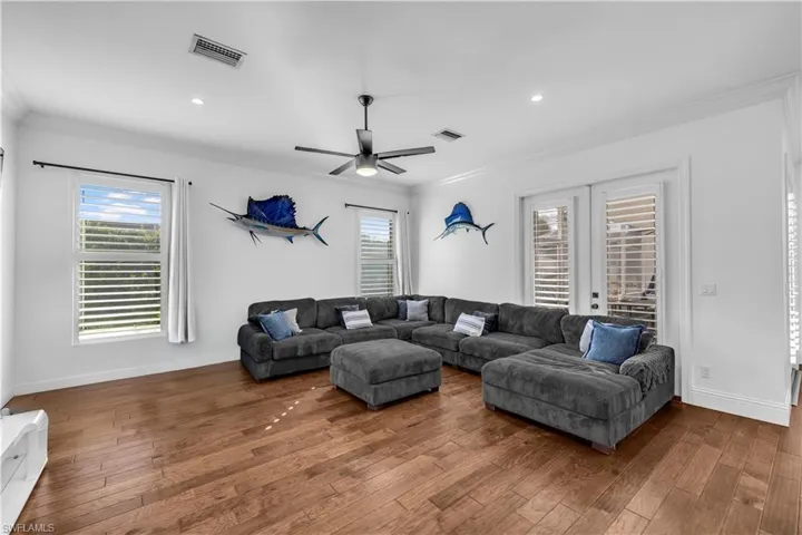Living room with dark wood-style flooring, crown molding, a ceiling fan, recessed lighting, and french doors