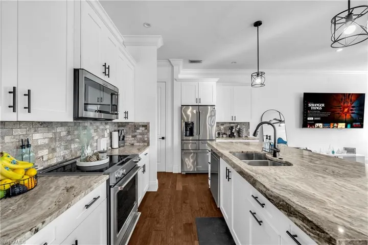 Kitchen featuring stainless steel appliances, light stone counters, white cabinetry, and crown molding