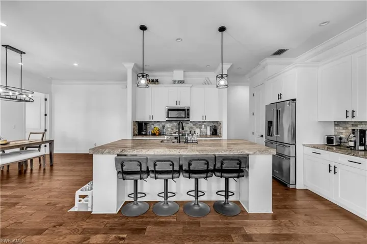Kitchen featuring a kitchen bar, hanging light fixtures, white cabinetry, stainless steel appliances, and decorative backsplash