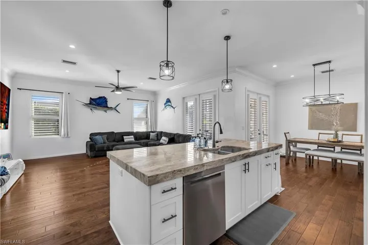 Kitchen with open floor plan, white cabinets, stainless steel dishwasher, pendant lighting, and dark wood-style floors