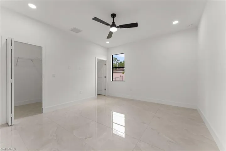 Unfurnished bedroom with a walk in closet, light marble finish floors, ceiling fan, and recessed lighting