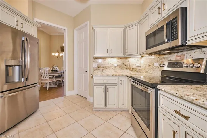 Kitchen with stainless steel appliances, a chandelier, light tile patterned floors, light stone countertops, and decorative backsplash