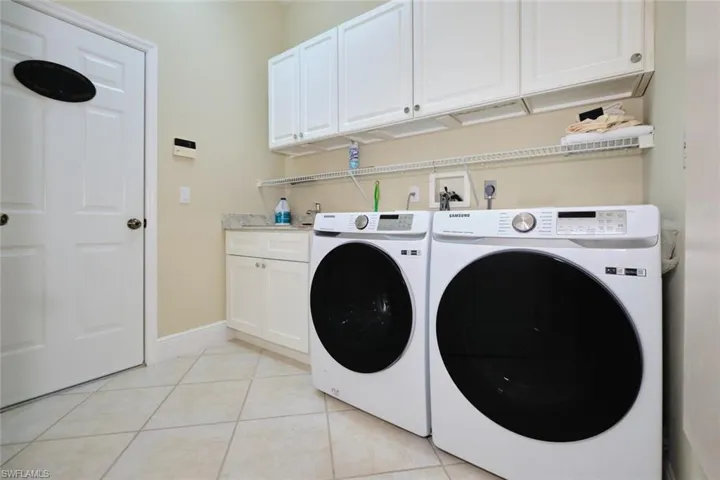 Laundry area featuring washing machine and clothes dryer, cabinet space, and light tile patterned flooring