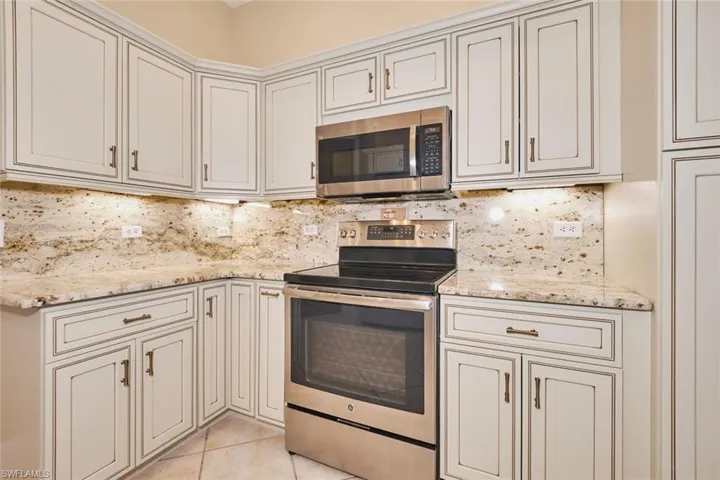 Kitchen featuring stainless steel appliances, light tile patterned flooring, light stone counters, and backsplash