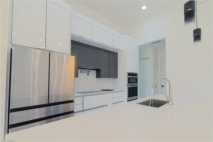 Kitchen featuring appliances with stainless steel finishes, white cabinets, modern cabinets, light stone countertops, and decorative light fixtures