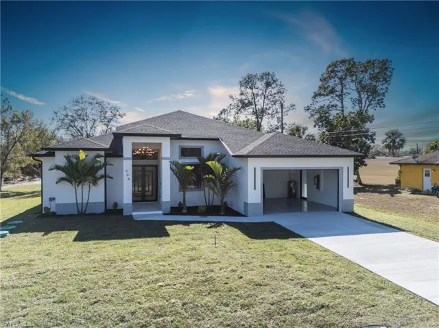 View of front of home with roof with shingles, a front yard, and stucco siding