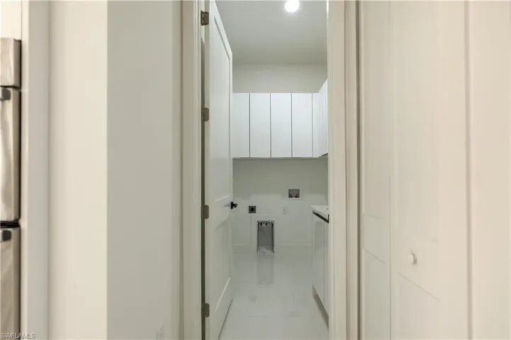 Laundry area with electric dryer hookup, light tile patterned flooring, hookup for a washing machine, and cabinet space