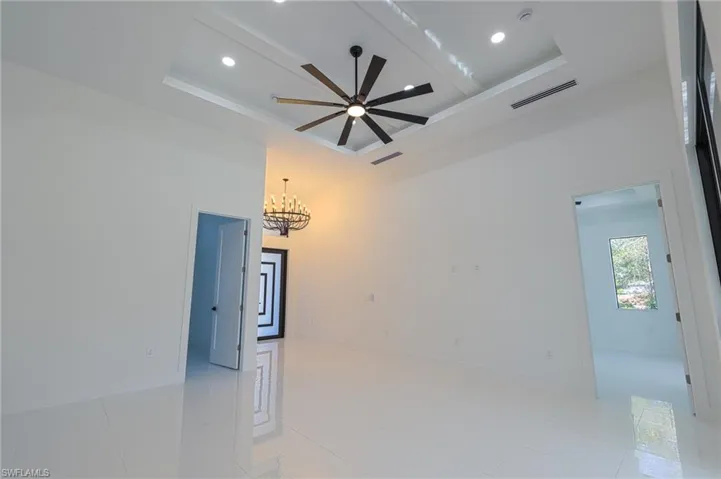 Unfurnished room featuring a chandelier, ceiling fan, light tile patterned floors, a tray ceiling, and a high ceiling