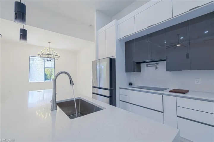 Kitchen with modern cabinets, freestanding refrigerator, white cabinets, decorative light fixtures, and light stone countertops