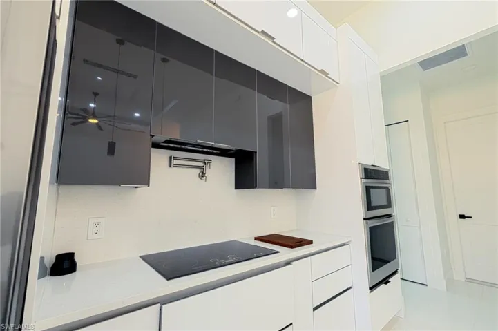 Kitchen featuring modern cabinets, black electric stovetop, light stone countertops, ceiling fan, and white cabinets