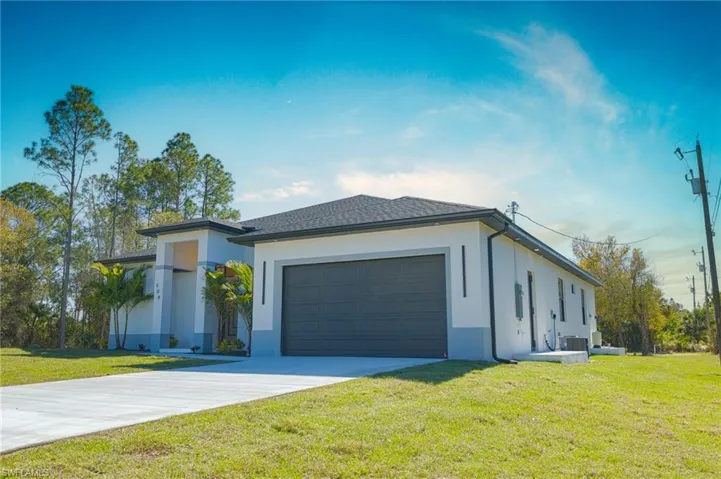View of front of house with a front yard, stucco siding, concrete driveway, and an attached garage