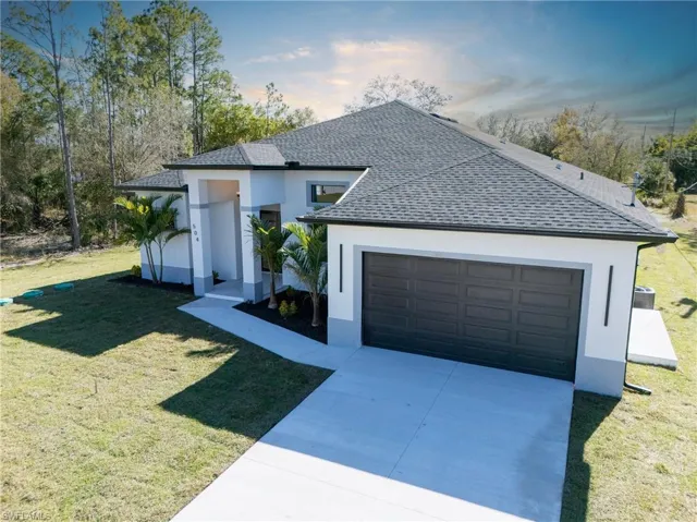 View of front of house with a yard, roof with shingles, driveway, and stucco siding