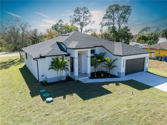 View of front facade featuring a front lawn, stucco siding, concrete driveway, roof with shingles, and a garage