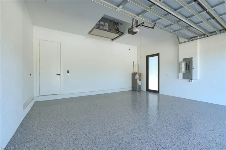 Garage with electric water heater, electric panel, and a garage door opener