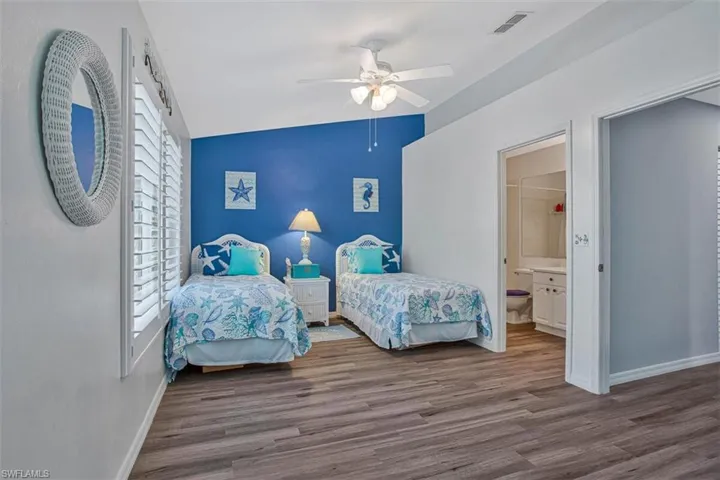 Bedroom featuring vaulted ceiling, wood finished floors, a ceiling fan, ensuite bath, and an accent wall