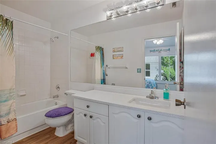 Ensuite bathroom featuring vanity, shower / bathtub combination with curtain, and wood finished floors