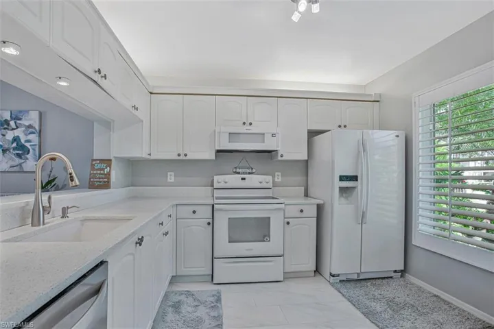 Kitchen featuring white appliances, white cabinetry, and light stone countertops