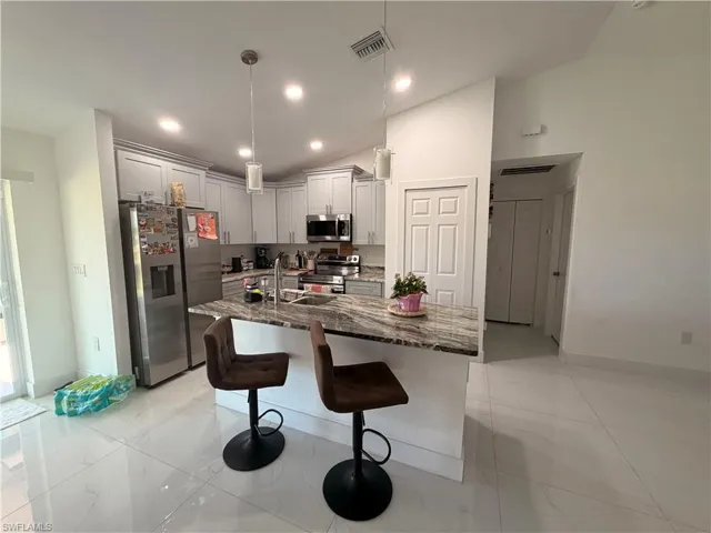 Contemporary kitchen featuring light gray cabinetry, stainless steel appliances, and a central island with a stone-finish countertop