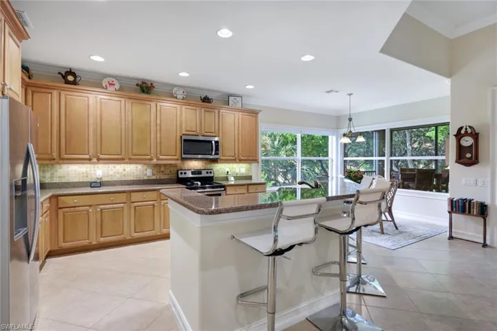 Kitchen featuring appliances with stainless steel finishes, dark stone countertops, pendant lighting, a center island with sink, and ornamental molding