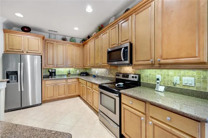 Kitchen with decorative backsplash, light stone counters, light tile patterned floors, stainless steel appliances, and ornamental molding
